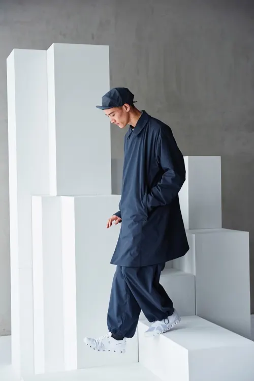 Man in oversized navy outfit descending white block steps, minimal, photographic, dark