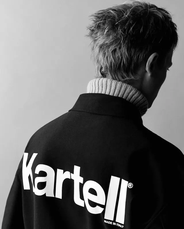 Back view of person wearing black Kartell jacket with white logo, minimal, photographic, monochrome