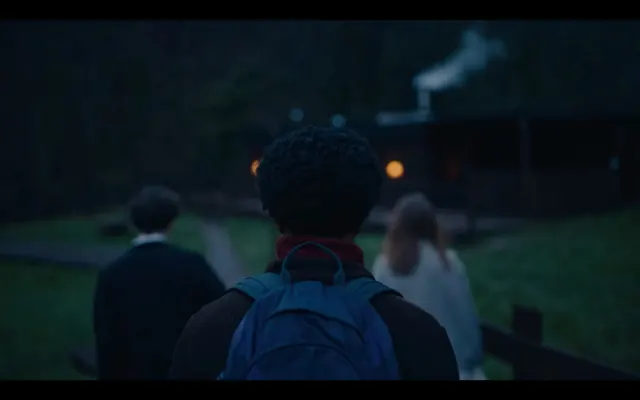Back view of person with backpack approaching cabin at dusk, photographic, dark, dark