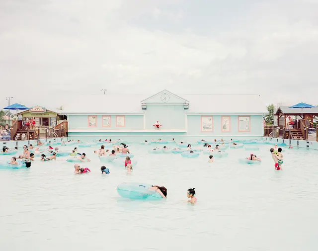 Crowded swimming pool with blue inner tubes at water park, photographic, playful, light
