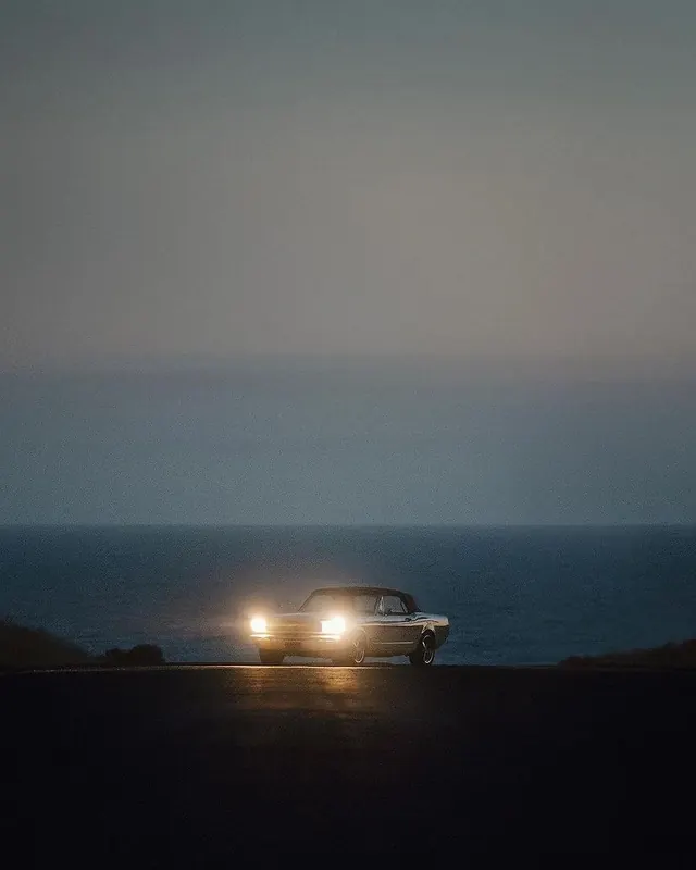 Vintage car at dusk by the ocean, photographic, dark