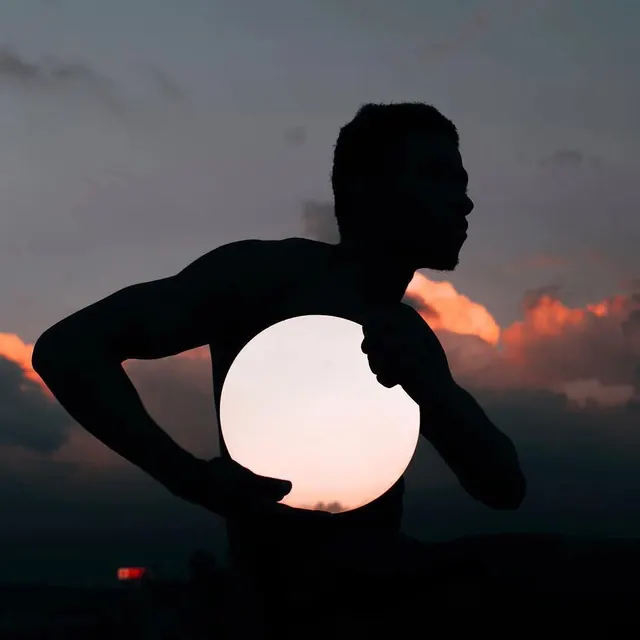 Silhouette holding glowing orb at dusk, photographic, minimal, dark
