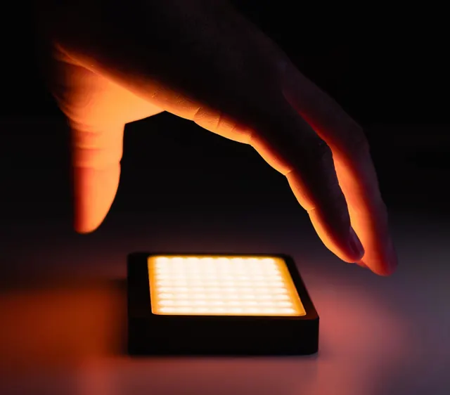 Hand over orange LED panel, photographic, minimal, dark