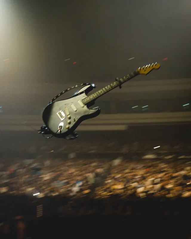 Guitar mid-air over concert crowd, photographic, editorial, dark