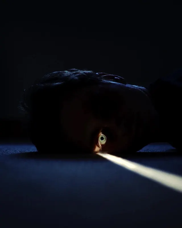 Single eye in diagonal spotlight, photographic, minimal, dark
