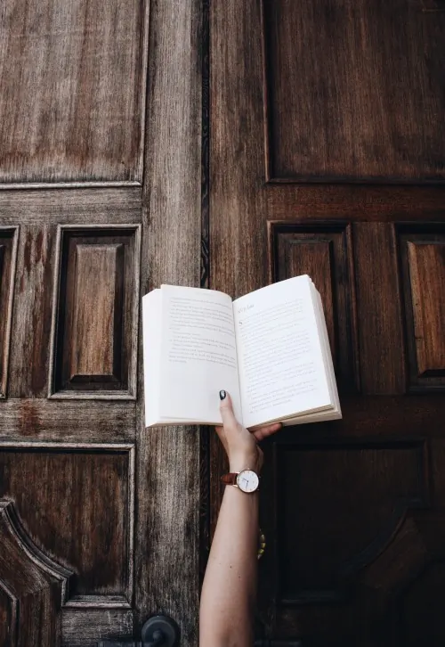 Hand Holding Open Book Against Wooden Door, photographic, minimal, dark