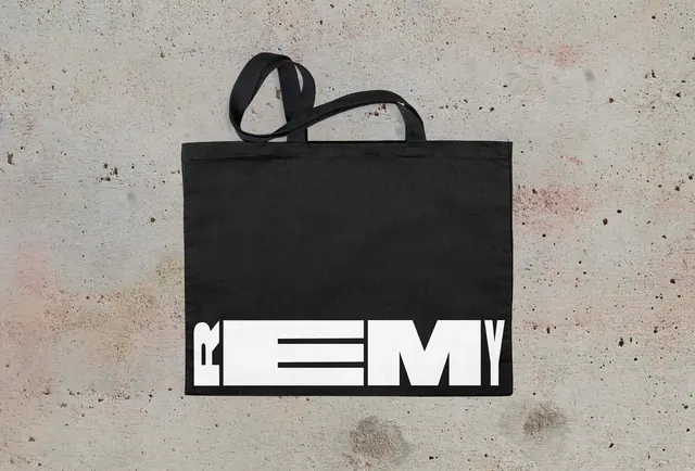 Black tote bag with bold white REMY logo, minimal, monochrome, dark