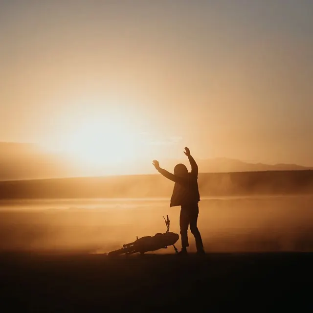 Silhouetted rider with motorcycle at sunset, photographic, minimal, warm