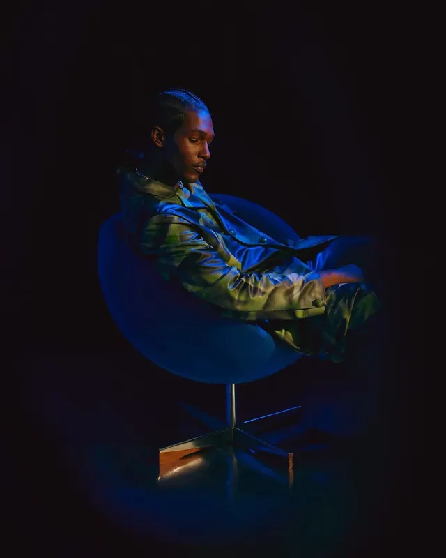 Man in Futuristic Jacket Seated in Blue Chair