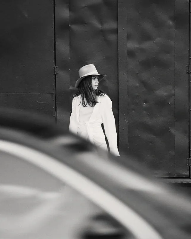Fashion model in wide-brim hat against industrial metal (B&W), photographic, editorial, monochrome