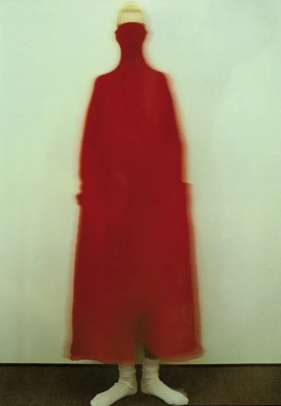 Blurred figure in flowing red coat against light wall, photographic, abstract, warm