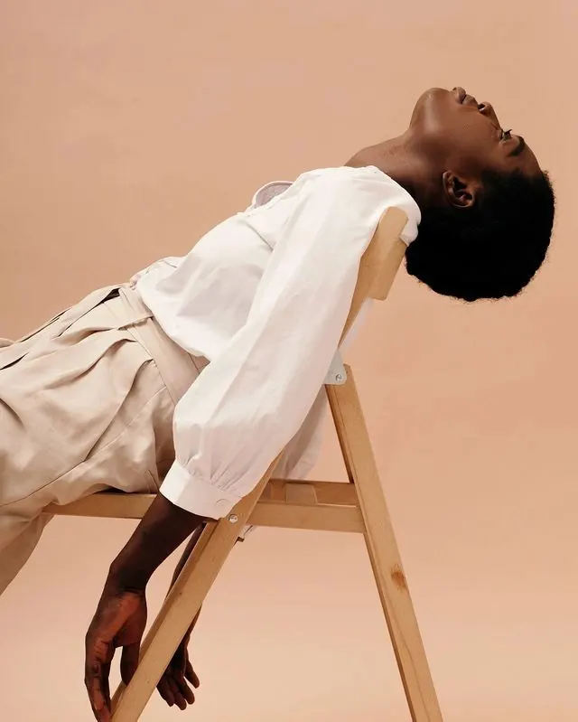 Peach studio fashion pose on wood chair, editorial, minimal, warm