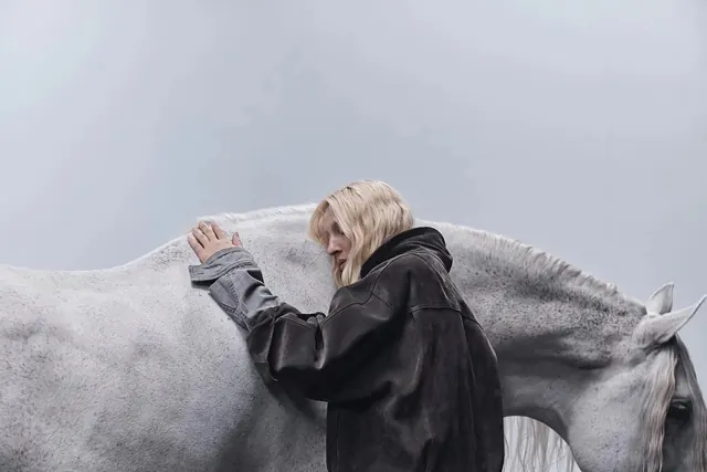 Woman resting head against white horse, editorial, photographic, muted