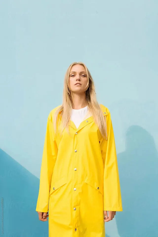 Yellow raincoat portrait on blue wall, minimal, photographic, light