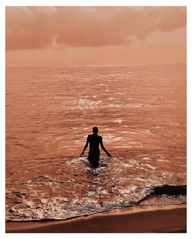 Silhouette wading into sea, minimal, photographic, warm