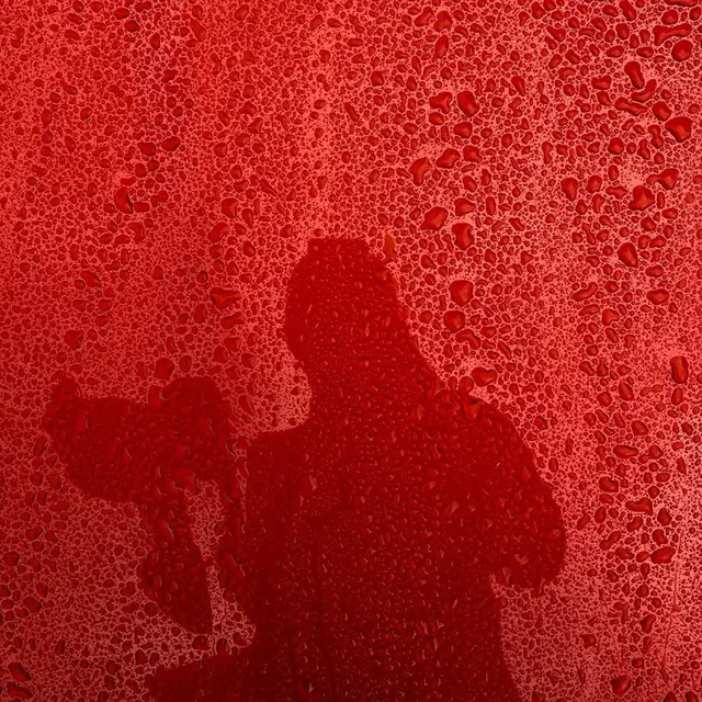 Red water-beaded surface with photographer shadow, minimal, photographic, vibrant