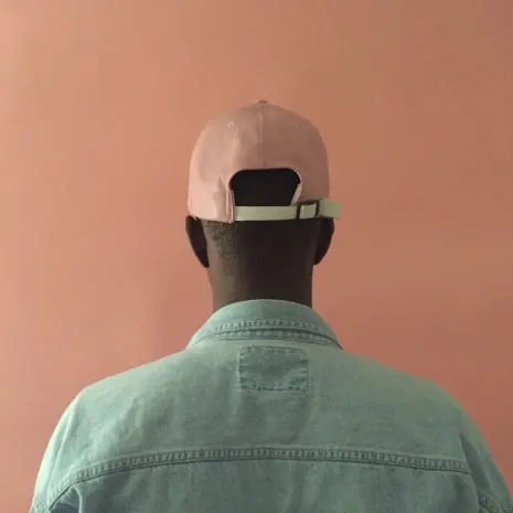 Back-view cap and denim on rose wall, minimal, photographic, muted