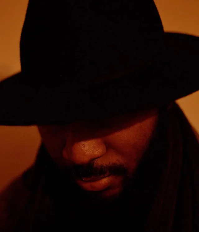 Low-key portrait under wide black hat, photographic, minimal, dark
