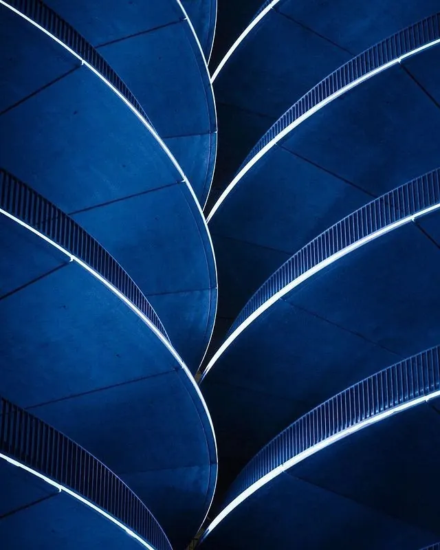 Blue-lit repeating concrete spiral ramps, geometric, photographic, dark