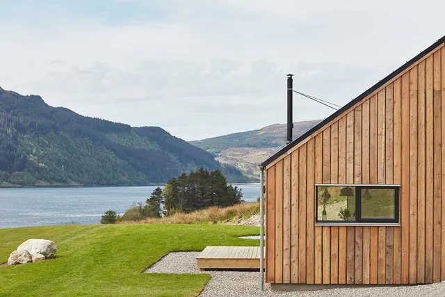Wood-clad lake house on green lawn, minimal, photographic, light