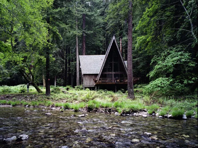 A-frame cabin in a forest by a river