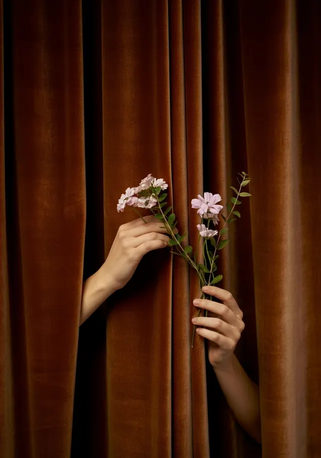 Hands Holding Flowers Against Velvet Curtain