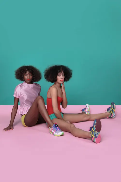 Two women in colorful outfits against a pink and teal background