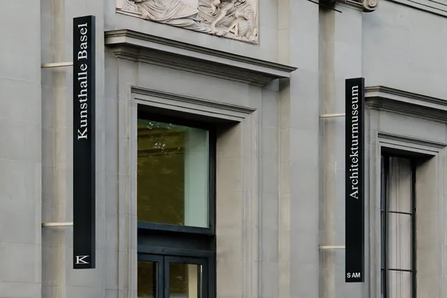 Vertical museum signage on stone facade, minimal, editorial, muted