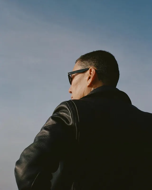 Profile portrait of man in leather jacket and sunglasses, minimal, photographic, dark