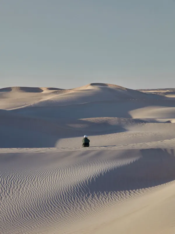 Lone figure seated in expansive sand dunes, minimal, photographic, light