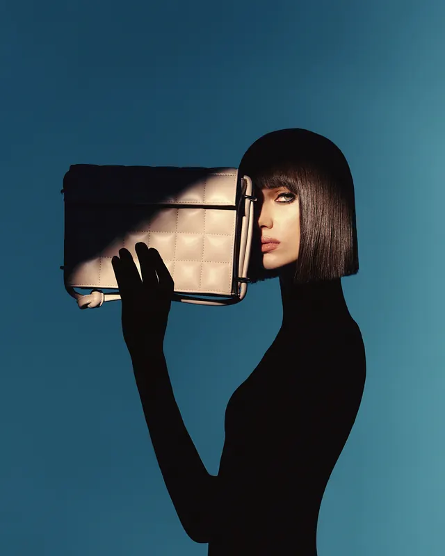 Fashion model holding quilted handbag against blue, minimal, photographic, cool