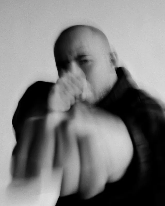 Motion blurred portrait of bald man with raised hand, minimal, photographic, monochrome