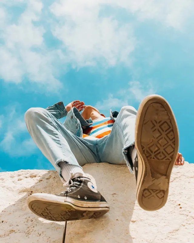 Low angle person lying on stone in denim and sneakers, photographic, light
