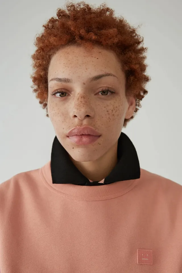 Portrait of model with curly red hair in peach sweatshirt, photographic, minimal, warm