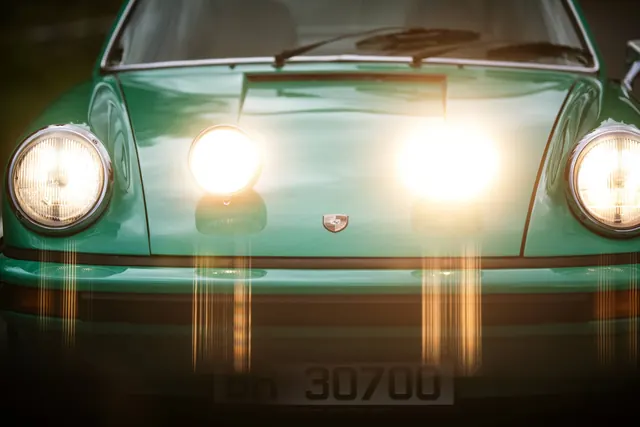 Vintage green Porsche headlight close-up, photographic, warm