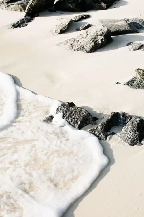 Wave foam on white sand with dark rocks, photographic, minimal, light