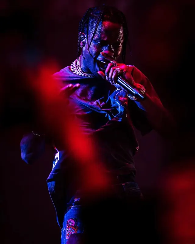 Travis Scott performing on stage under red lights, photographic, energetic, vibrant