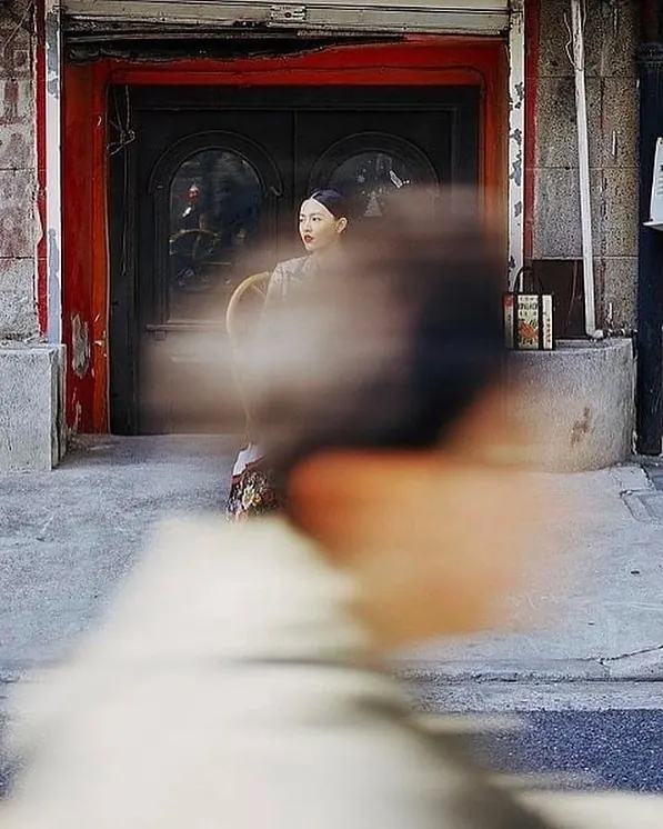 Street scene with blurred figures and red storefront, photographic, dark