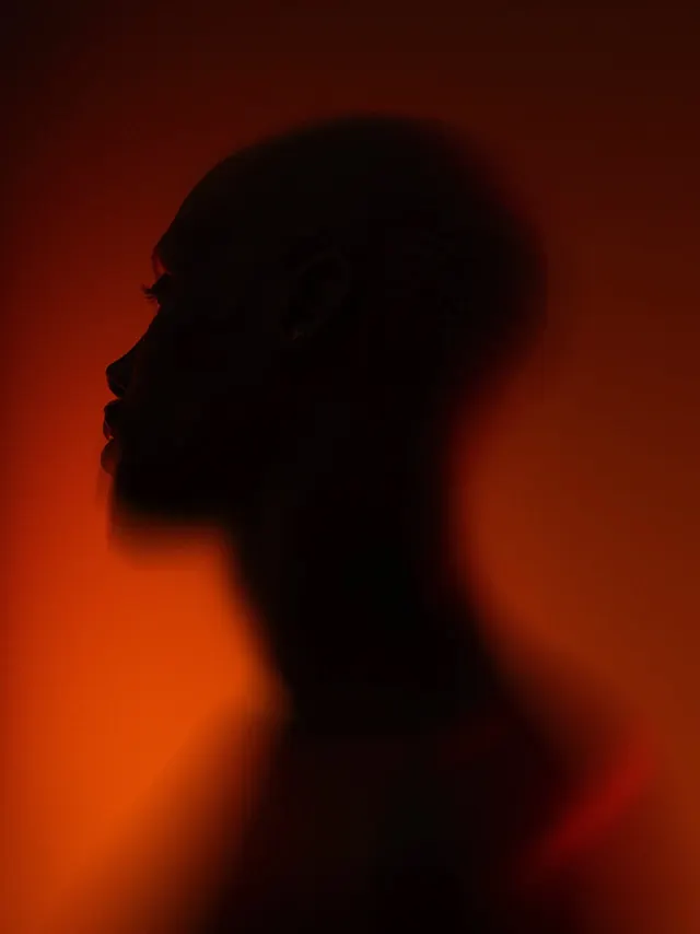 Silhouette portrait with warm red gradient backdrop, photographic, minimalist, warm