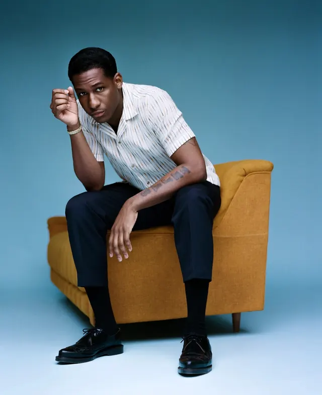 Portrait on mustard chair against blue background, photographic, light-mode, warm