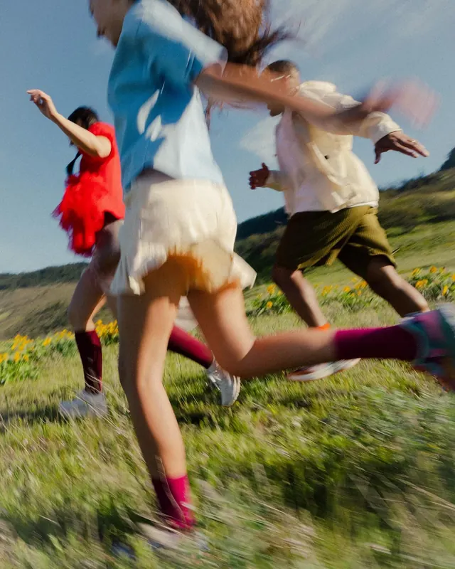 Figures in motion across sunlit wildflower field, photographic, editorial, warm