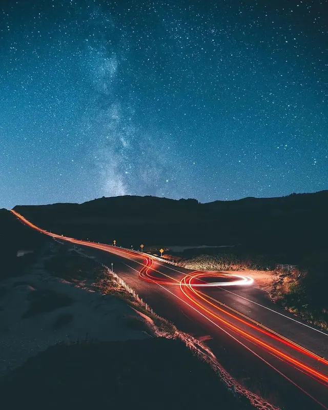 Winding mountain road at night with red light trails and starry sky, photographic, dark