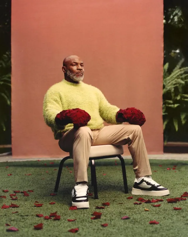 Seated figure with red roses against coral wall, photographic, minimalist, warm
