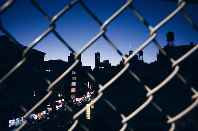 City lights through chain-link fence, photographic, technical, dark
