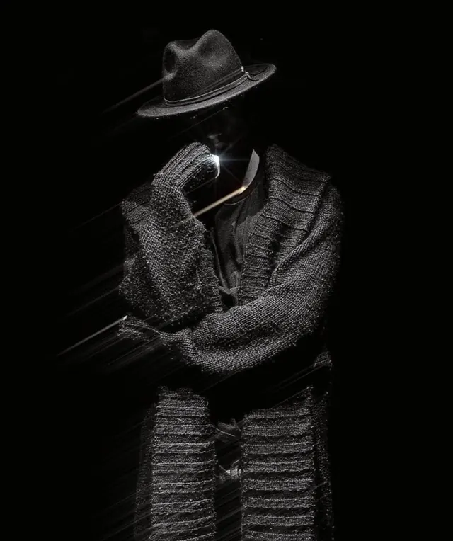 Figure in dark textured clothing against black, photographic, dark-mode, dark