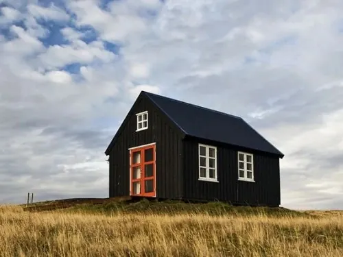 Black wooden house with orange door in field, photographic, minimalist, dark