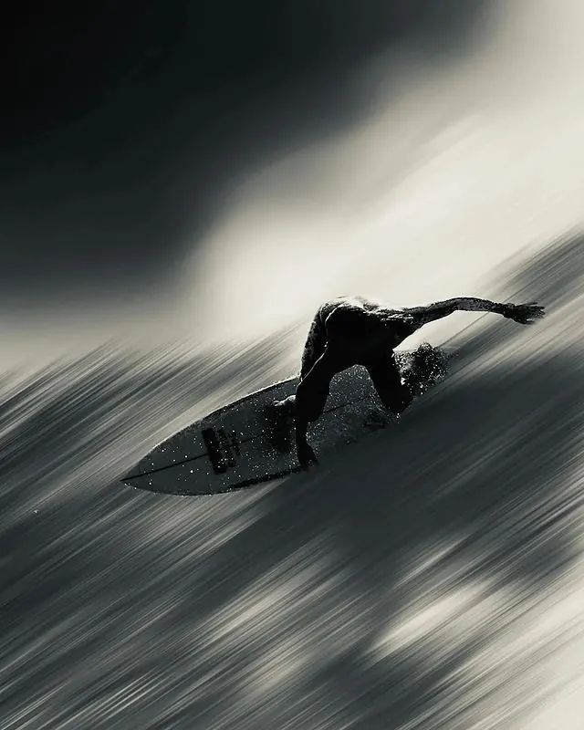 Silhouetted surfer with long-exposure ocean motion, photographic, minimalist, monochrome