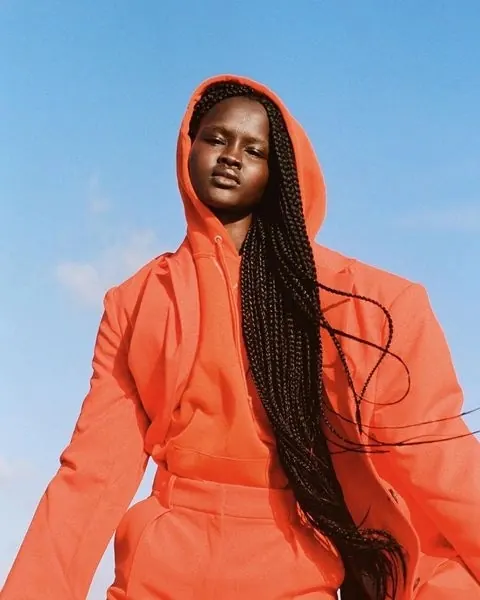 Portrait in orange hooded jacket against blue sky, photographic, minimal, vibrant