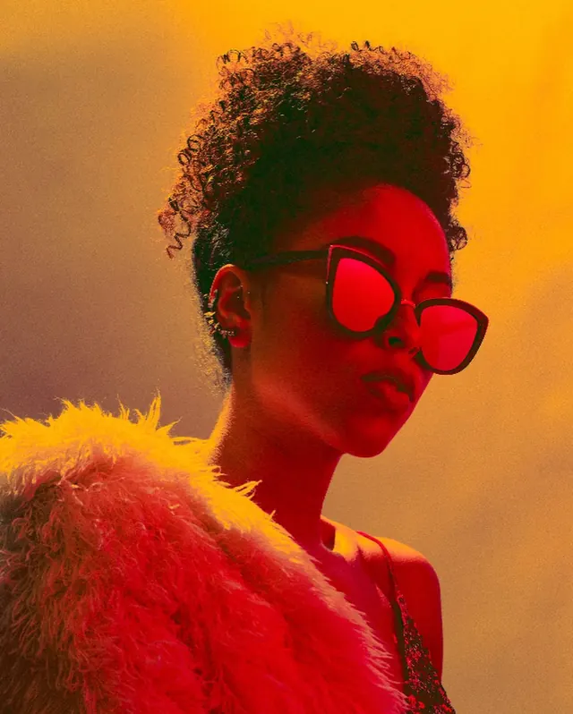 Portrait with oversized red sunglasses and orange gradient background, photographic, gradient-heavy, warm