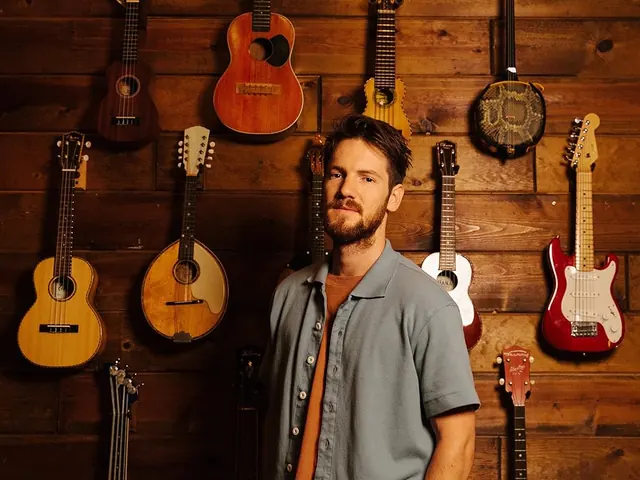 Musician in studio with wall-mounted guitar collection, photographic, editorial, warm